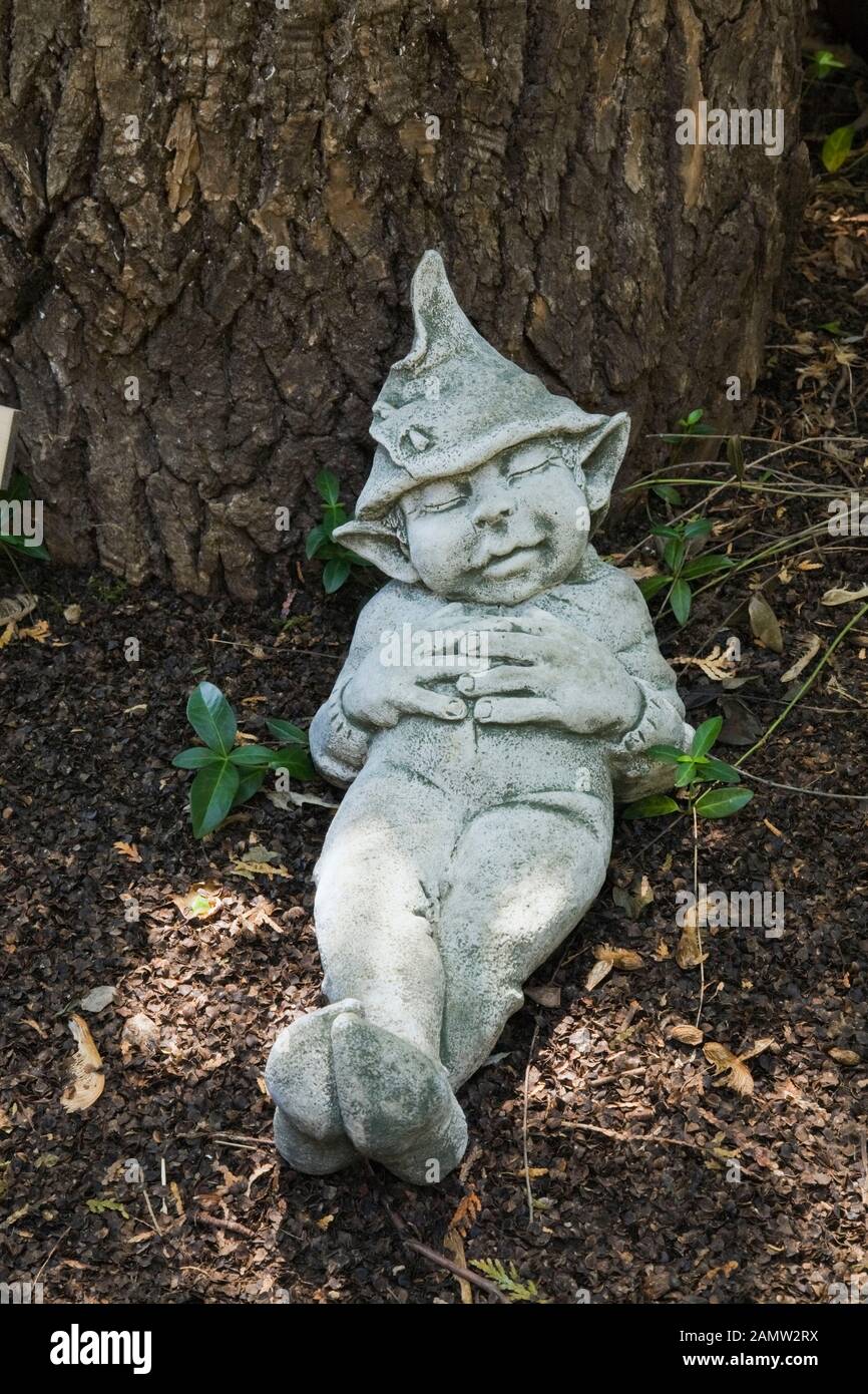 Statuette di dormire leprechaun accanto al tronco di albero nel giardino di campagna cortile in estate, l'art du Jardin giardino, Saint-Laurent, Ile d'Orleans, Quebec Foto Stock