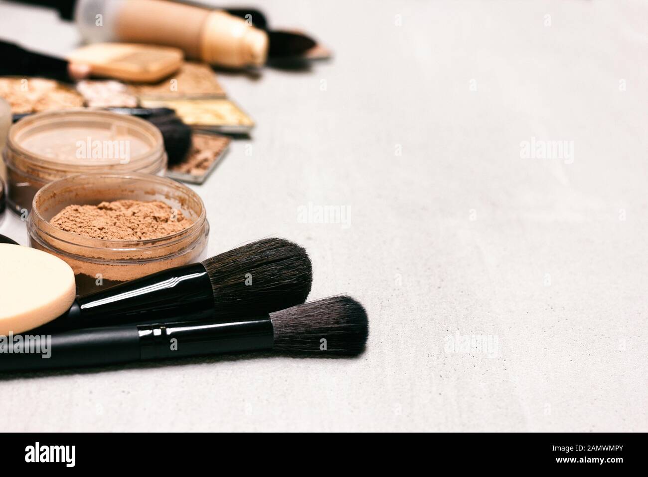 Sfondo per il trucco. Make-up in polvere, foundation, correttore con spazzole e spugne cosmetiche su una superficie in calcestruzzo con copia spazio - Vista laterale Foto Stock