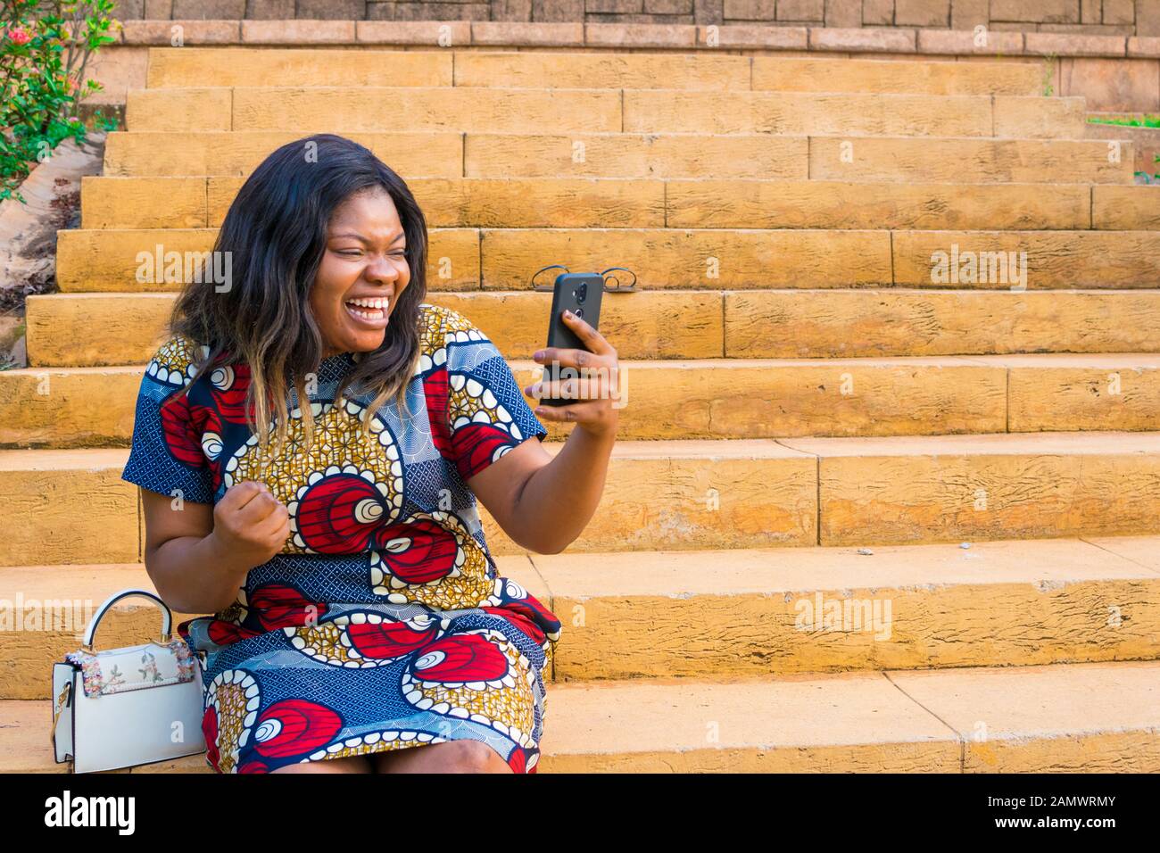 Giovane donna africana la visualizzazione di qualcosa sul suo telefono, sensazione di entusiasti, celebrando Foto Stock