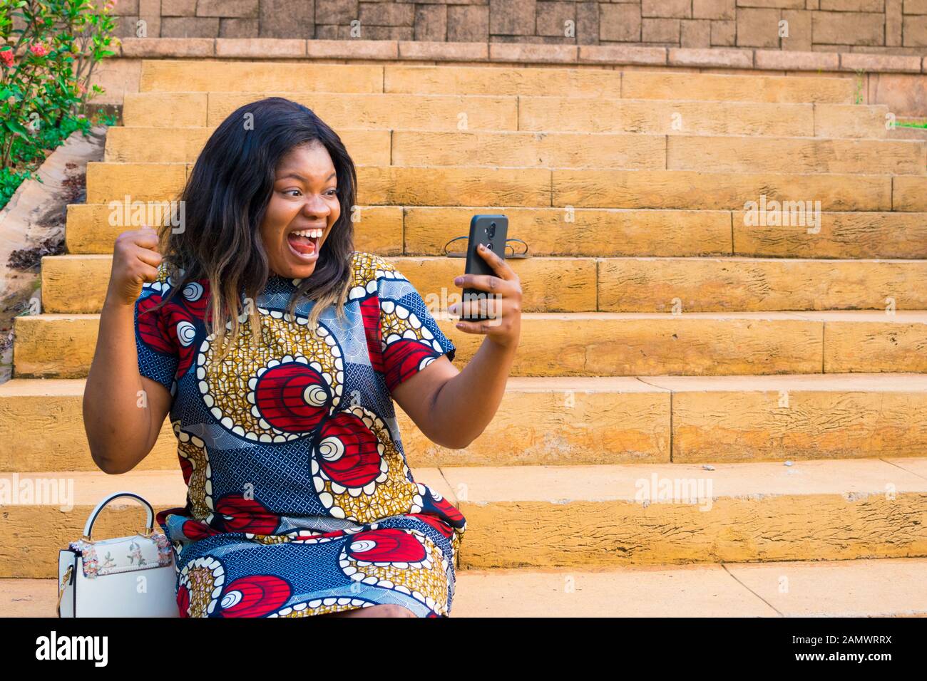Giovane donna africana la visualizzazione di qualcosa sul suo telefono, sensazione di entusiasti, celebrando e felice Foto Stock