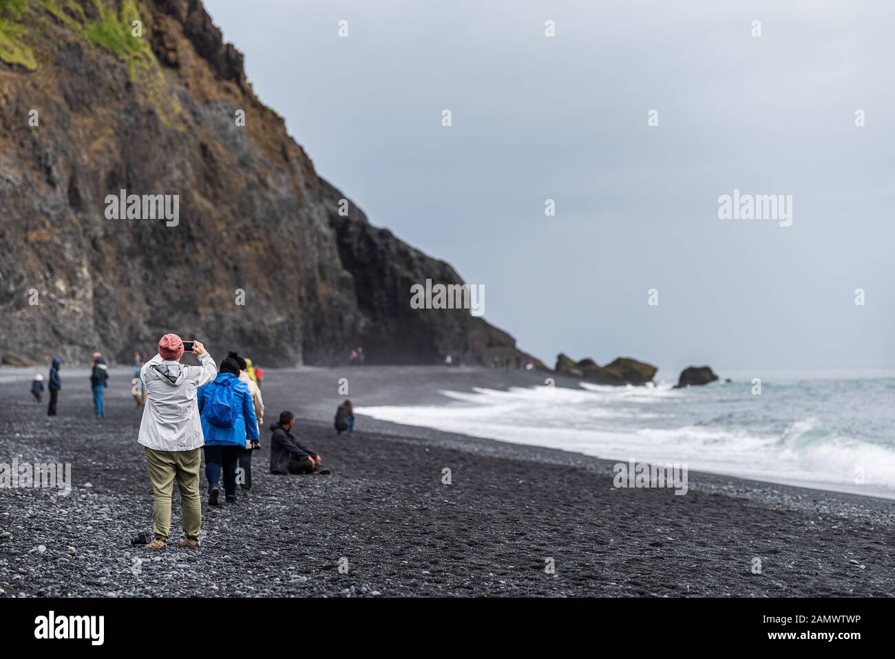 Myrdal, Islanda - 14 giugno 2018: Formazioni rocciose vulcaniche della spiaggia di sabbia nera di Reynisfjara, con persone che si affacciano sulla costa costiera che scattano foto Foto Stock
