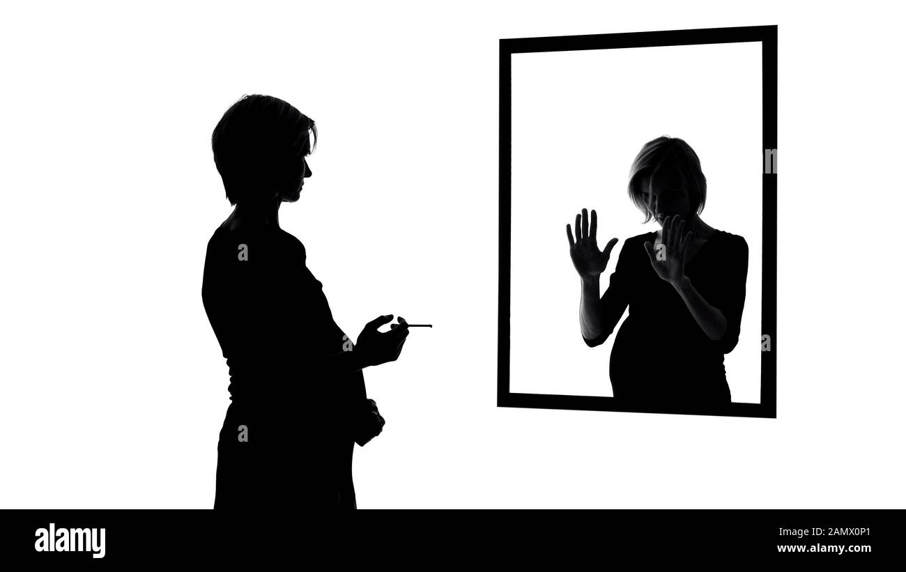 Donna incinta colpita dalla coscienza che fuma la sigaretta davanti allo specchio, abitudini Foto Stock