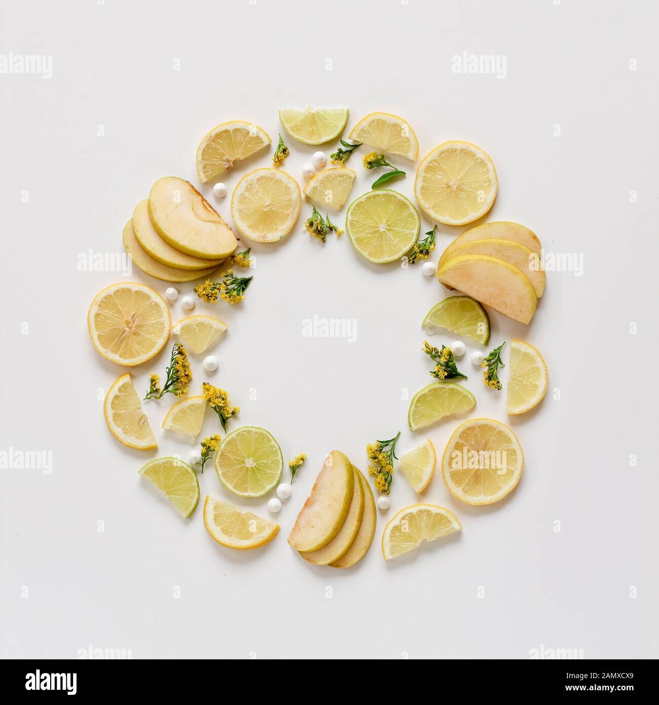 Modello creativo di frutta a fette e fiori gialli. Mela verde, limoni verdi e gialli disposti a cerchio. Disposizione piatta con spazio di copia Foto Stock