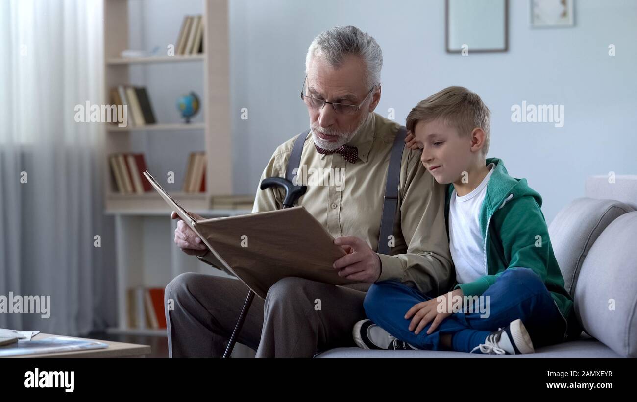 Gentile vecchio leggere fiaba a nipote, ragazzo docile appoggiato alla spalla Foto Stock