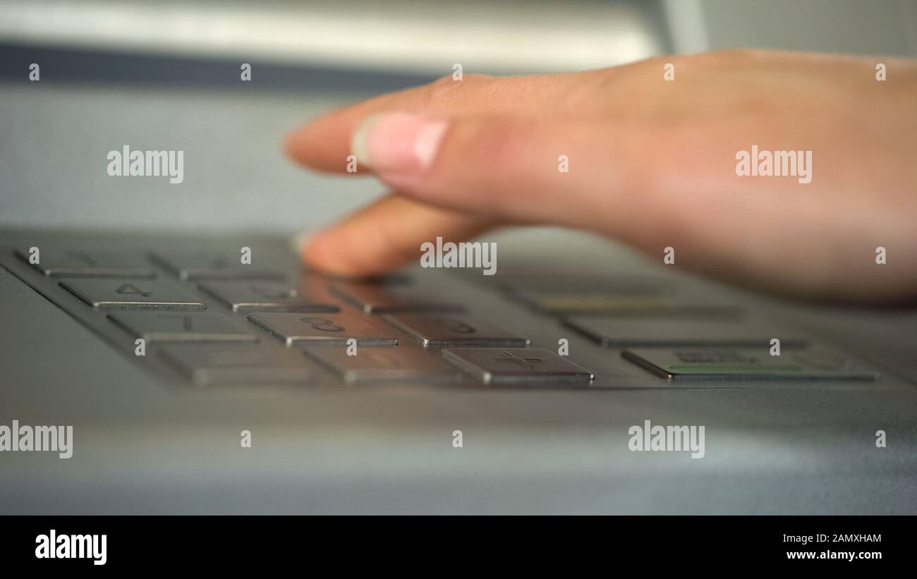 Mano femminile utilizzando ATM, inserendo codice personale univoco e premendo i pulsanti Foto Stock