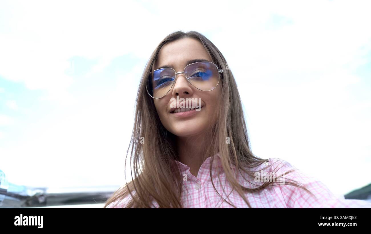 Elegante giovane donna in occhiali da sole sorridente contro il cielo, prendendo selfie, gioventù Foto Stock