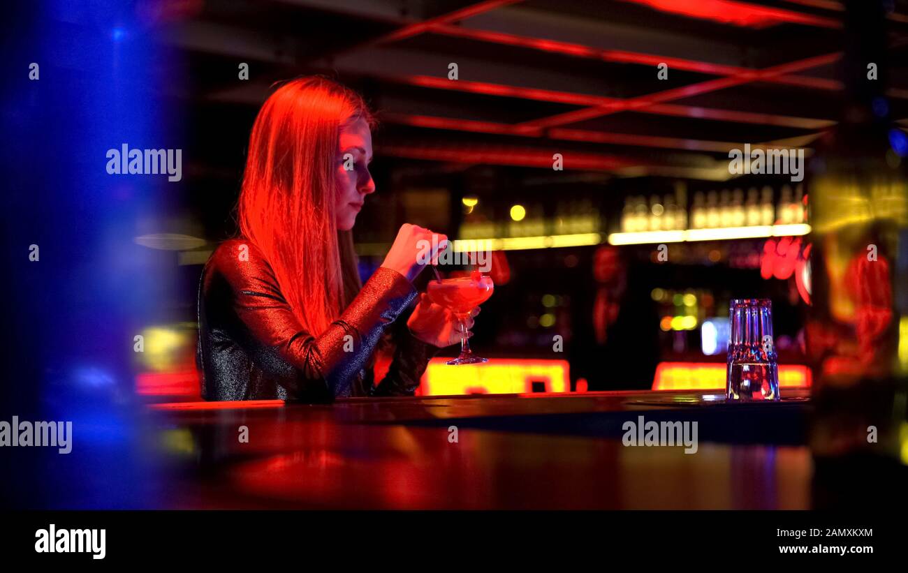 Bella giovane donna seduta e bere cocktail al party in discoteca Foto Stock