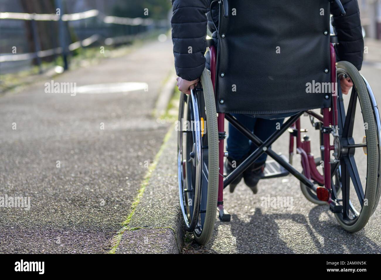 Basso angolo posteriore vista di una donna disabile su sedia a rotelle in una tranquilla strada in città in un concetto di mobilità e indipendenza per i portatori di handicap Foto Stock