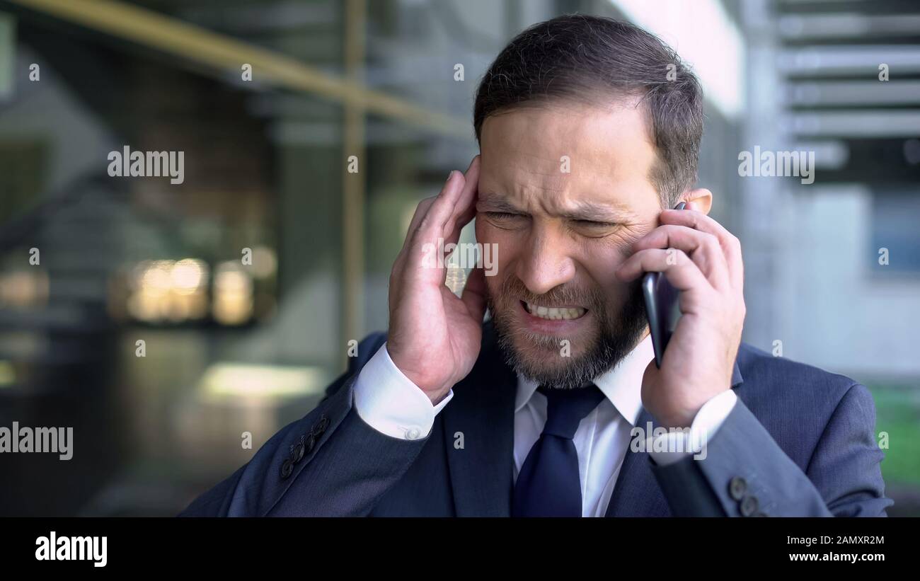 Superlavorato manager maschile parlando al telefono, soffre di emicrania, mal di testa Foto Stock