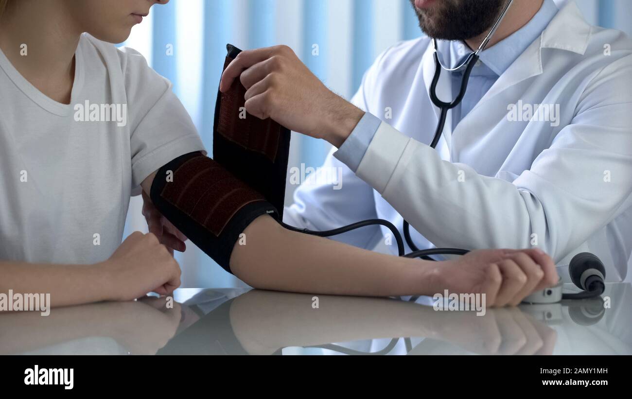 Terapeuta maschile che si prepara a misurare la pressione sanguigna della giovane donna, diagnostica Foto Stock