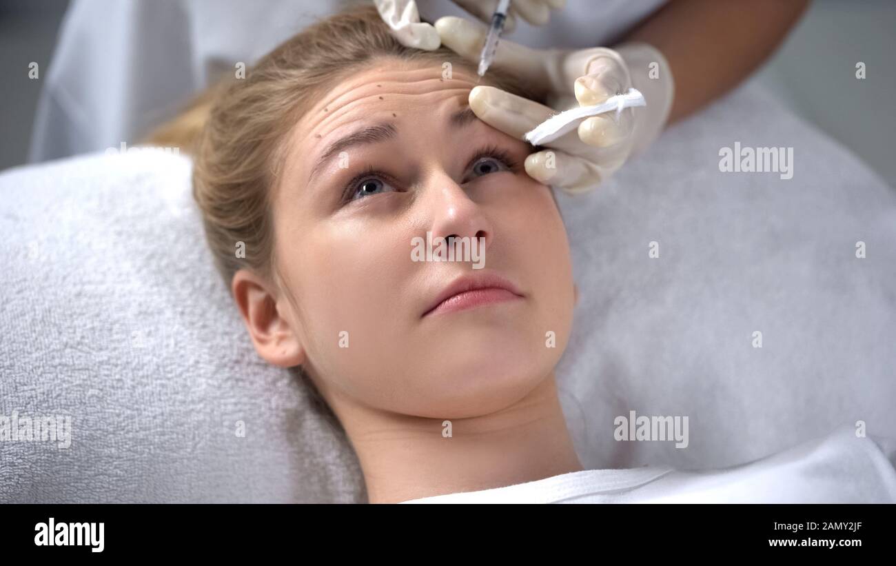 Cosmetologo che fa iniezione di botox a giovane donna, rughe lisciatura Foto Stock