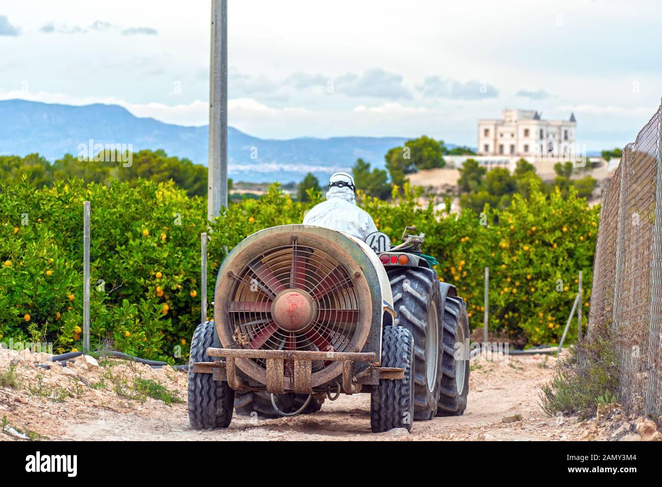 Agricoltore indossando indumenti protettivi rigidi di un trattore su una piantagione di limoni in Spagna. Agricoltore circa a spray antiparassitario e insetticida. Weed insetticida f Foto Stock