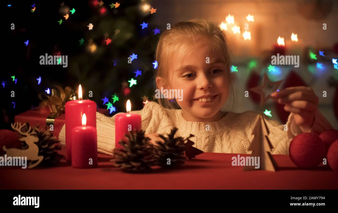 Felice ragazza sorridente giocando vicino scintillante albero X-mas, arredamento in legno per le vacanze Foto Stock