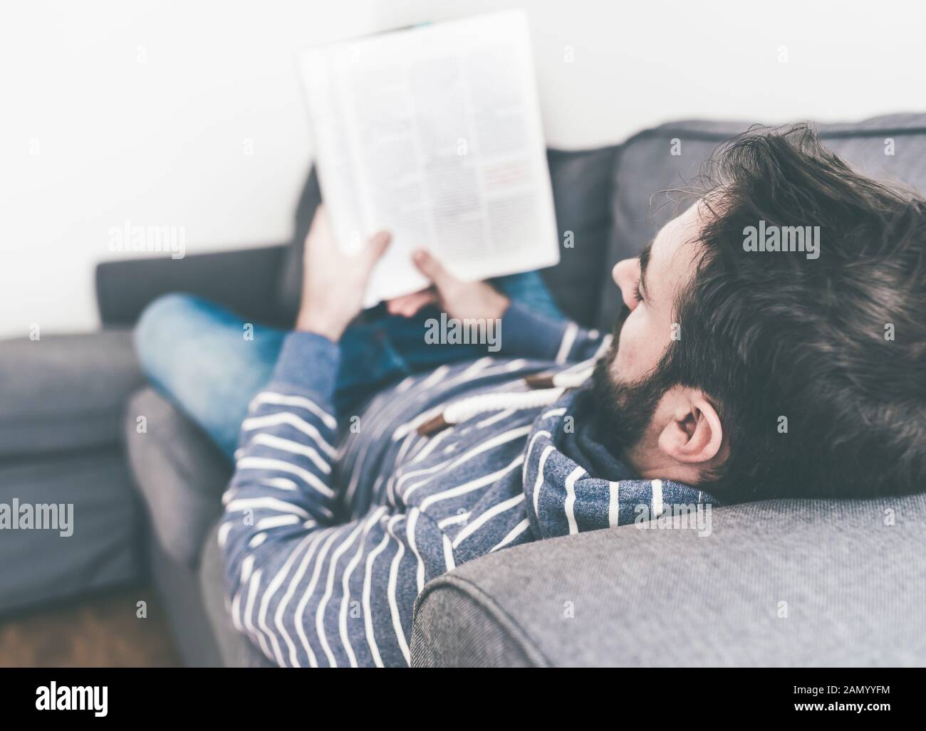l'uomo si rilassa sul divano mentre legge la rivista o il giornale Foto Stock