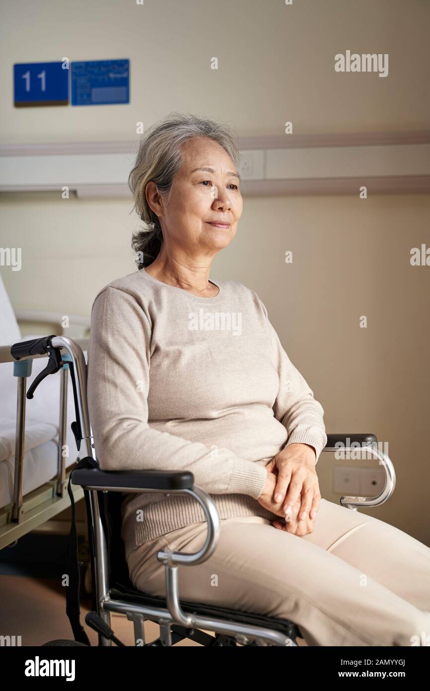 donna anziana asiatica seduta in sedia a rotelle nella sua stanza in casa di cura con espressione facciale vuota Foto Stock