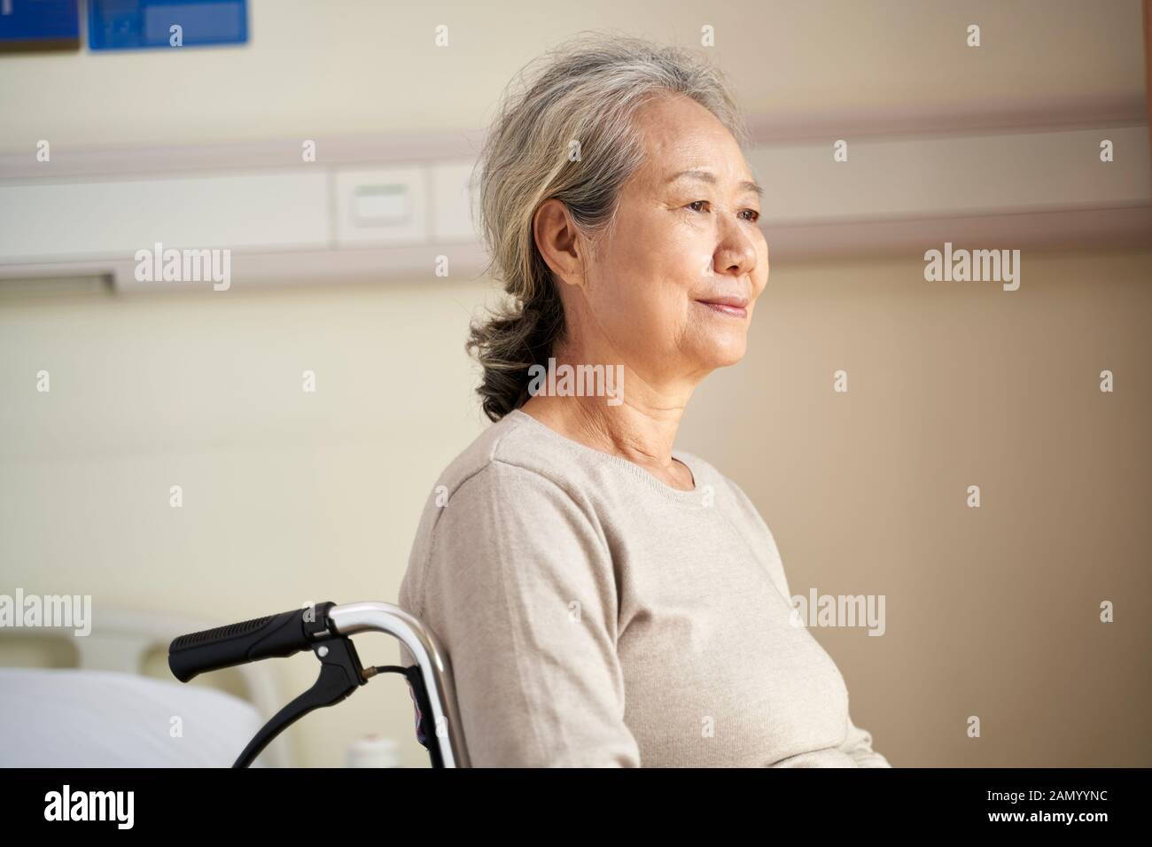 contenuto asian anziano donna seduta in sedia a rotelle nella sua stanza in casa di cura con espressione facciale pacifica Foto Stock