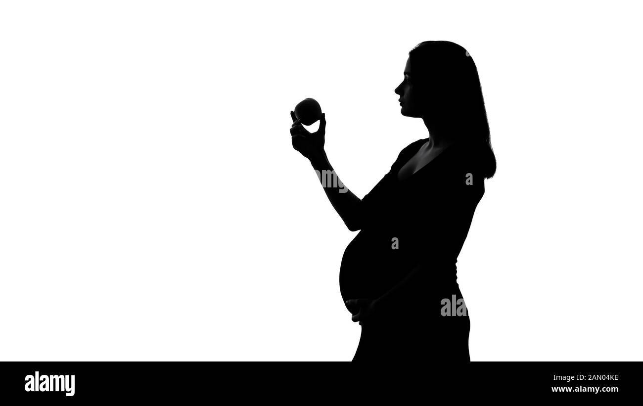 Silhouette di donna incinta mangiare mela, dieta sana durante il periodo di gravidanza Foto Stock