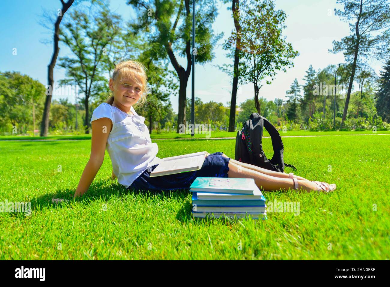 Una ragazza insegna le assegnazioni per i libri di testo e si siede sul prato verde nel parco. Foto Stock