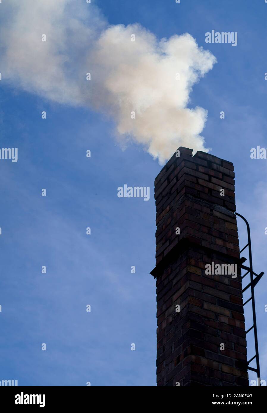 fumo in bilding / uscita dal camino di casa su sfondo cielo blu. Riscaldamento non ecologico delle famiglie. Riscaldamento invernale, oneri ambientali. Foto Stock