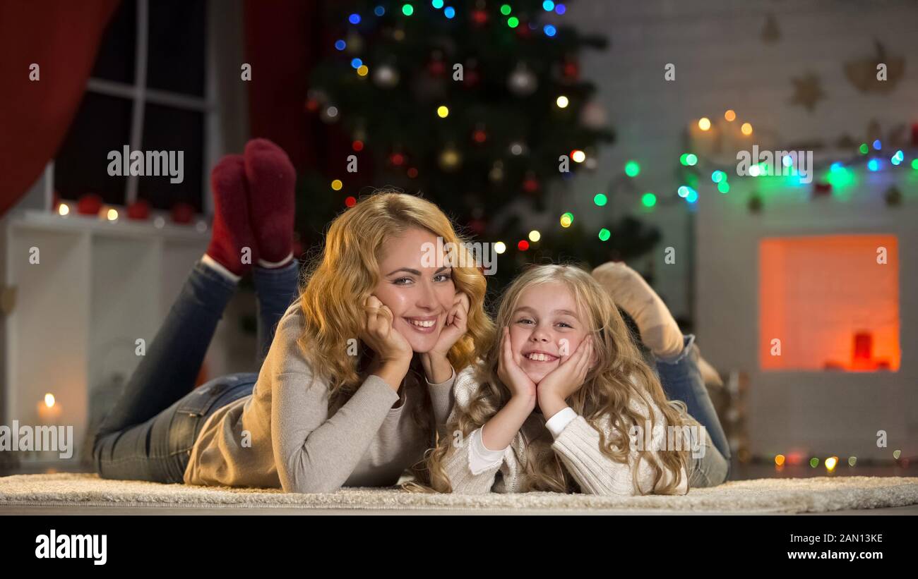 Giovane donna e ragazza sdraiata sotto l'albero di Natale, sorridente alla macchina fotografica, vacanze Foto Stock