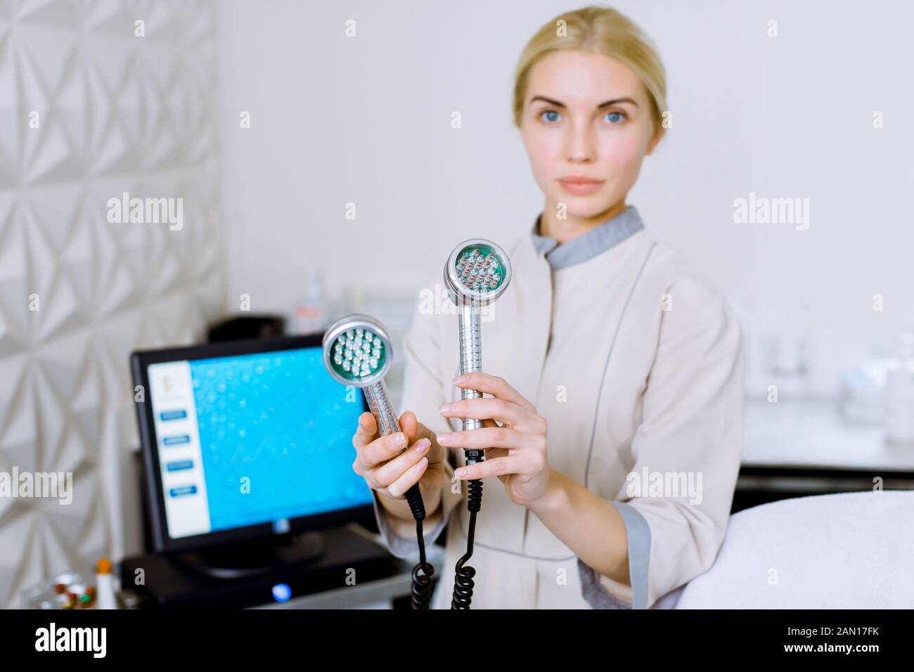 Bella donna bionda medico cosmeolotgist ed estetista tenendo un attrezzo per la mesoterapia LED luce fotonica RF terapia di ringiovanimento cutaneo, in piedi Foto Stock