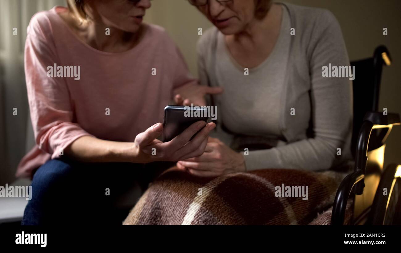 Genere volontario femminile che mostra la vecchia donna in sedia a rotelle come utilizzare lo smartphone Foto Stock