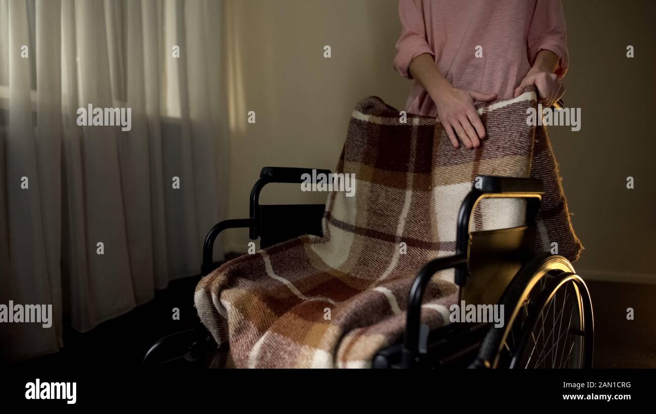 Figlia che accarezza la sedia a rotelle vuota con dolore, ricordando la madre è scomparsa Foto Stock