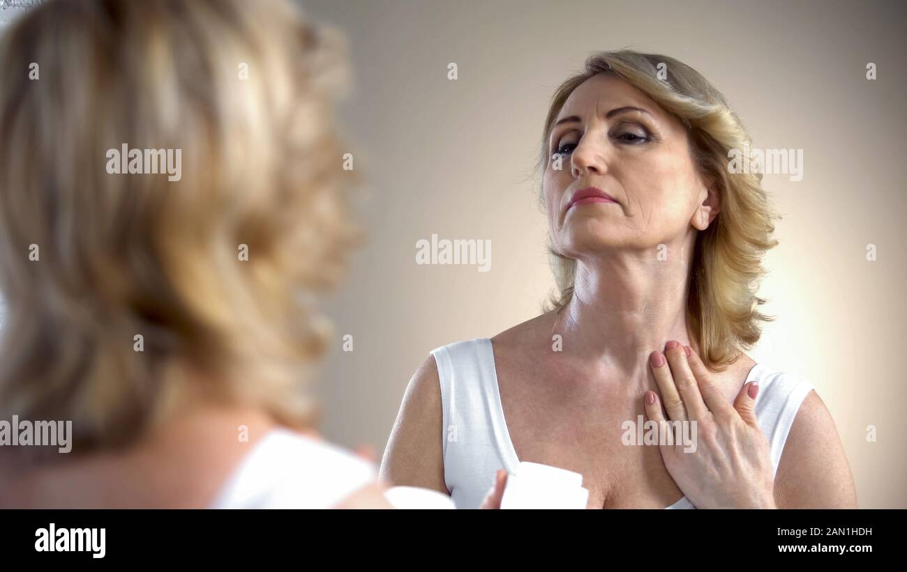 Vecchia donna che applica crema nutriente sul collo e sulla zona decolleta, cura anti-età Foto Stock