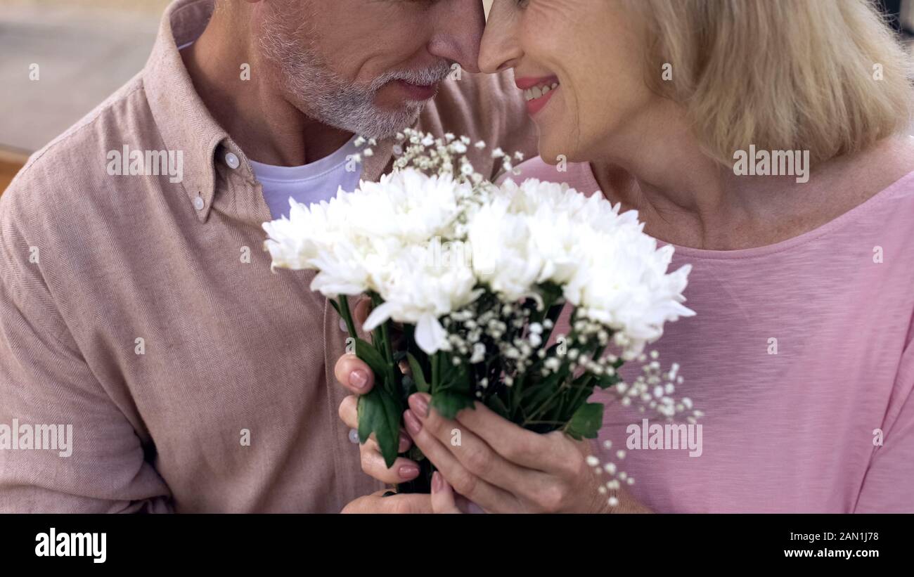 Felice coppia senior nuzzling, tenendo fiori mazzetto insieme, data anniversario Foto Stock