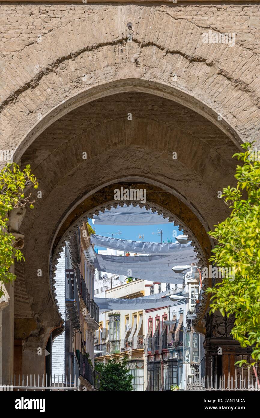 Il più archi a ferro di cavallo della Puerta del Jordon, nella Cattedrale di Siviglia, che conduce attraverso gli edifici e ombrelloni di Calle Hernando Colón. Foto Stock