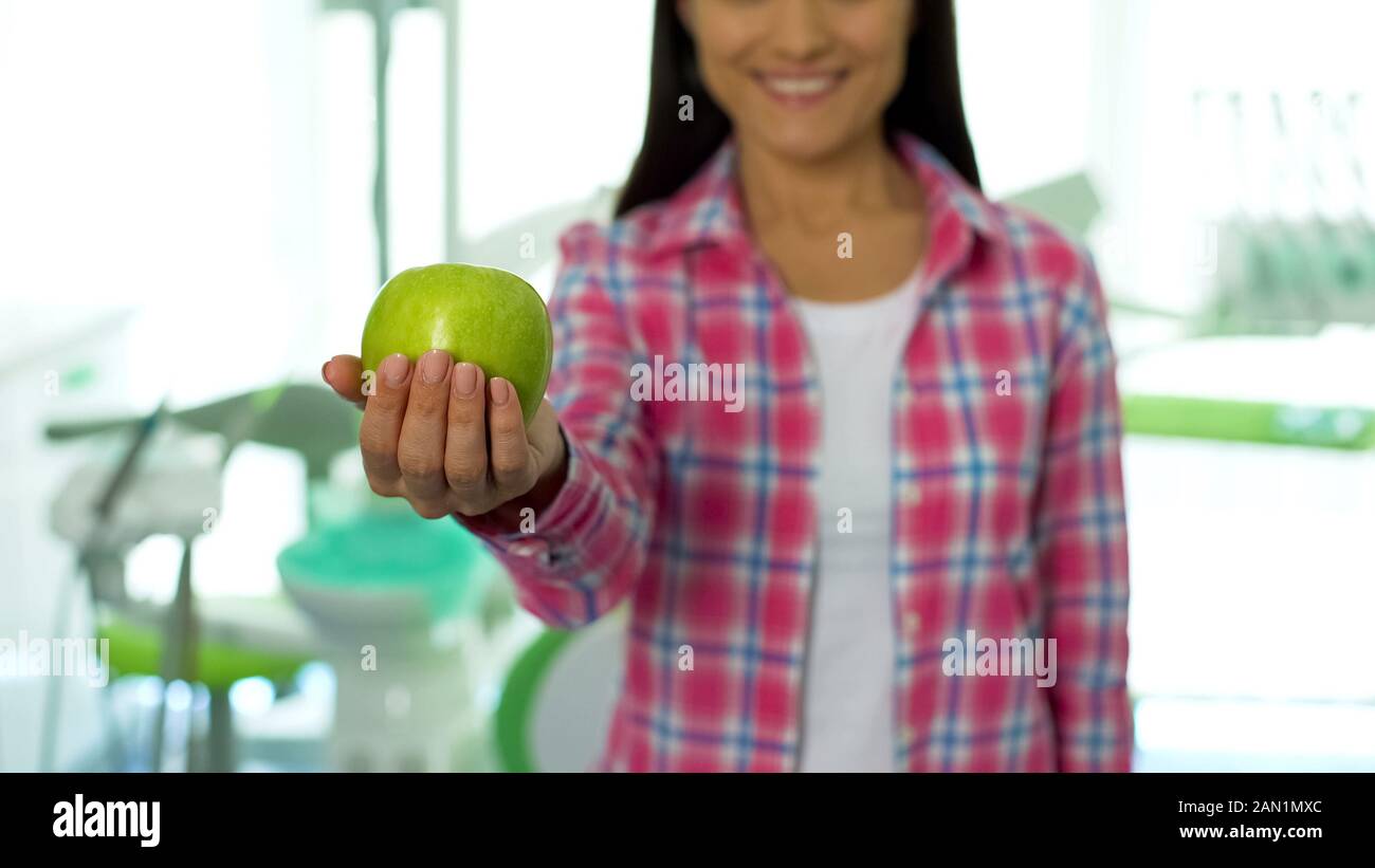 Bella ragazza che mostra mela verde a telecamera in studio dentistico, denti sani Foto Stock