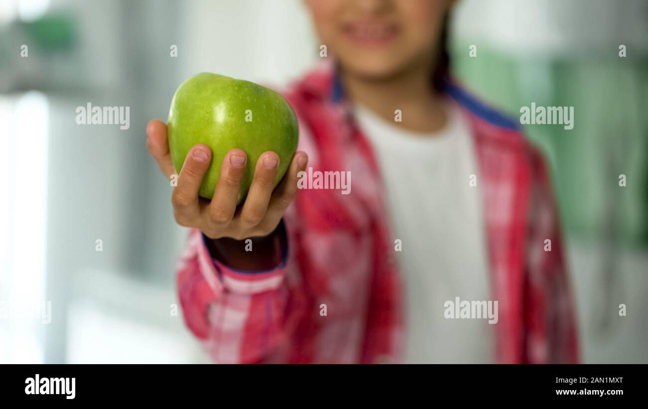 Sorridente kid mostra mela verde in telecamera, alimenti naturali per il concetto di assistenza sanitaria Foto Stock