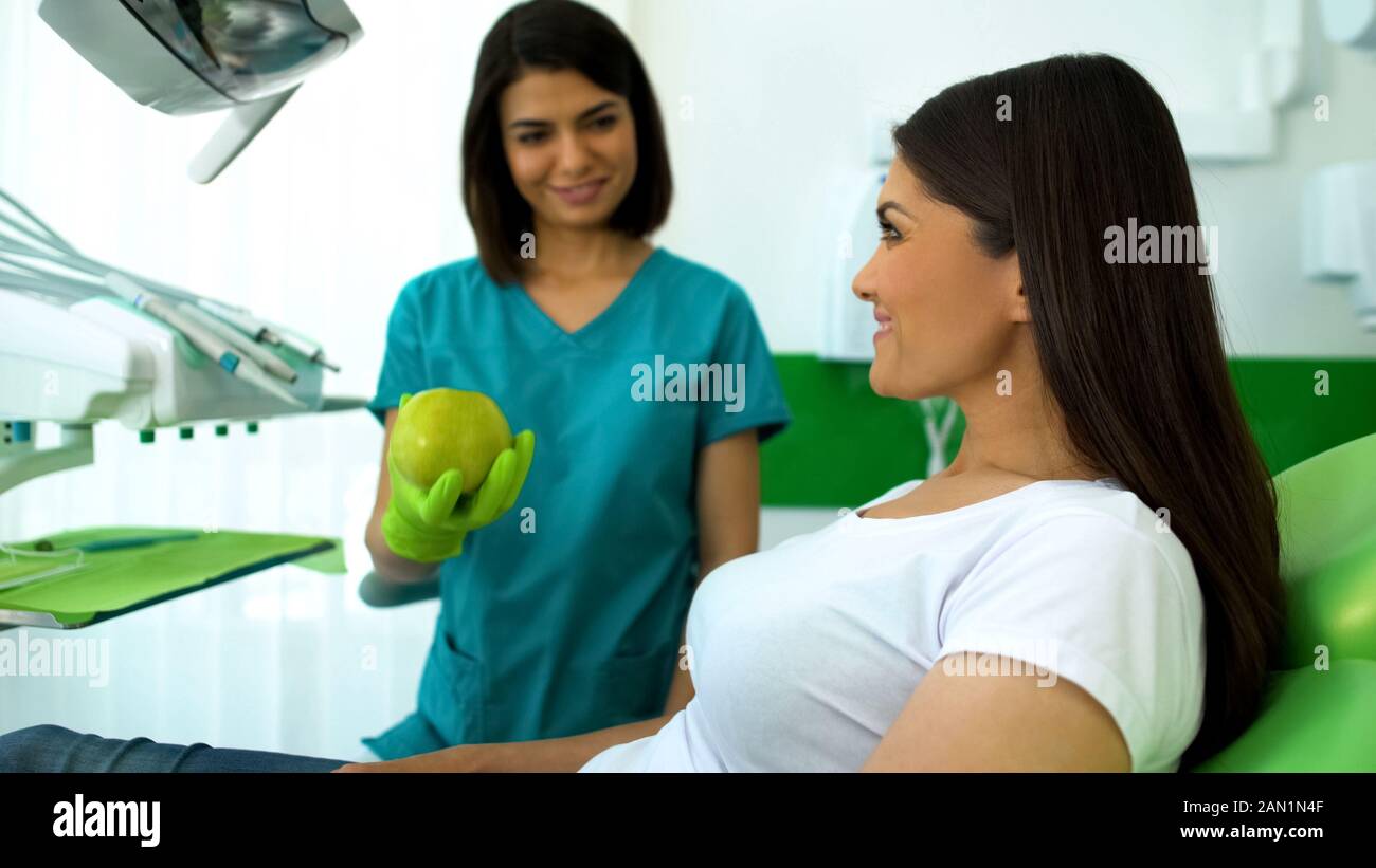 Signora sorridente dentista dando mela verde al paziente, raccomandazioni sanitarie Foto Stock