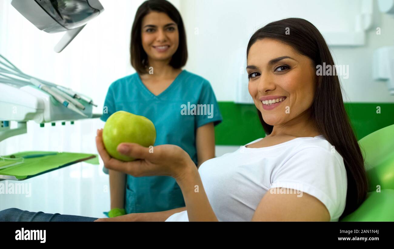 Signora paziente tenendo premuto mela verde e sorridente in telecamera professionale cura dei denti Foto Stock