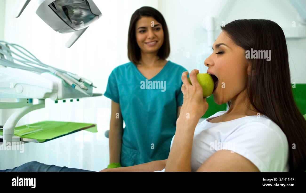 Signora stomatologist sorridente, guardando il paziente di mordere apple con i denti sani Foto Stock