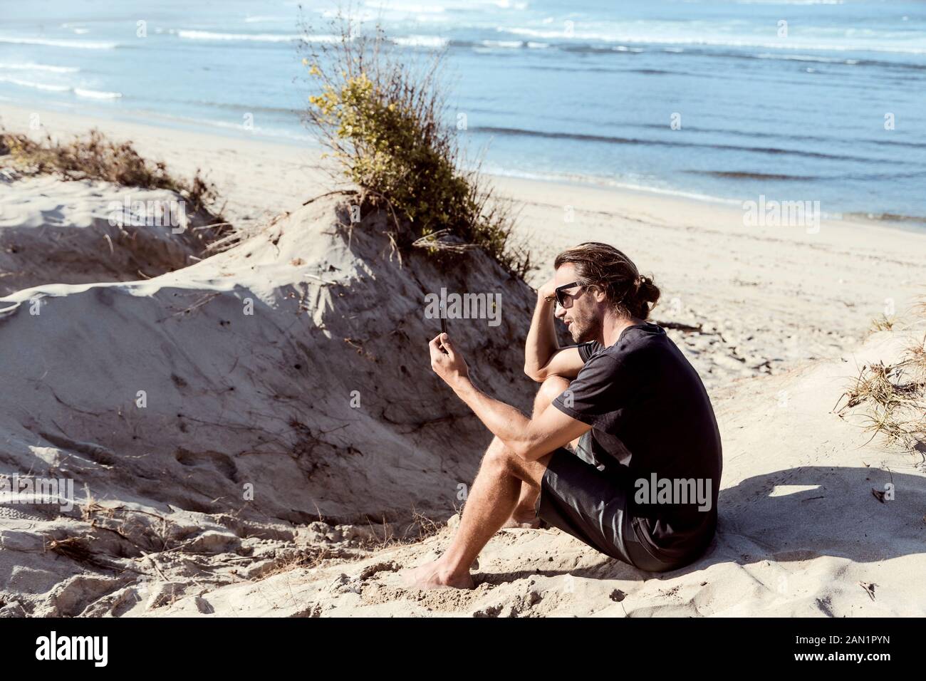 Uomo che usa lo smartphone sulla spiaggia Foto Stock