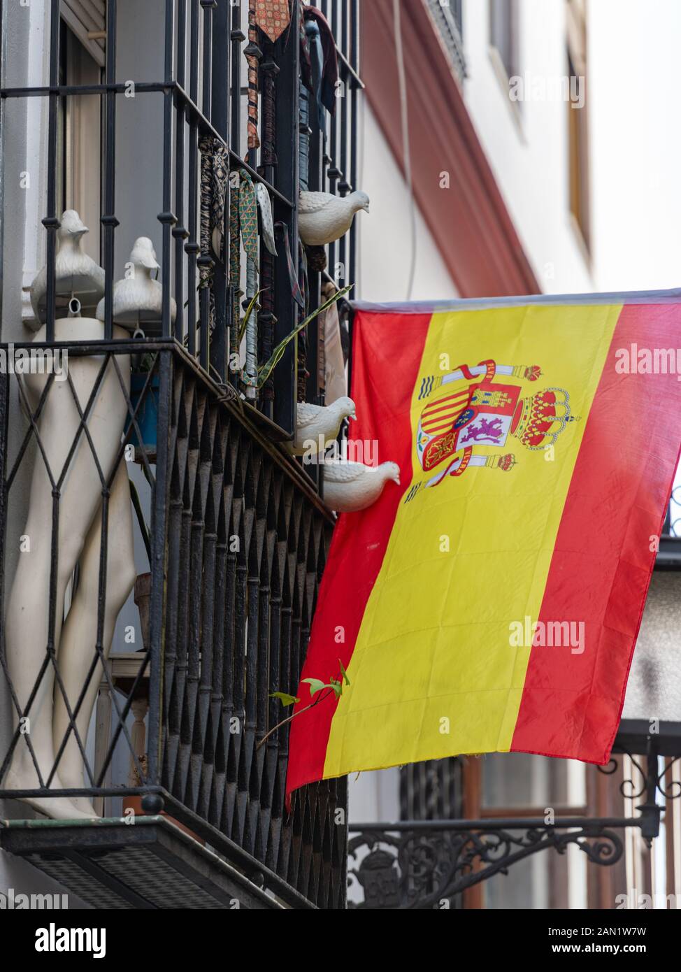 Una collezione di piccioni colati si affaccia su una bandiera spagnola appesa a un tradizionale balcone in ferro battuto di Siviglia con gambe e cravatte da uomo manichino. Foto Stock