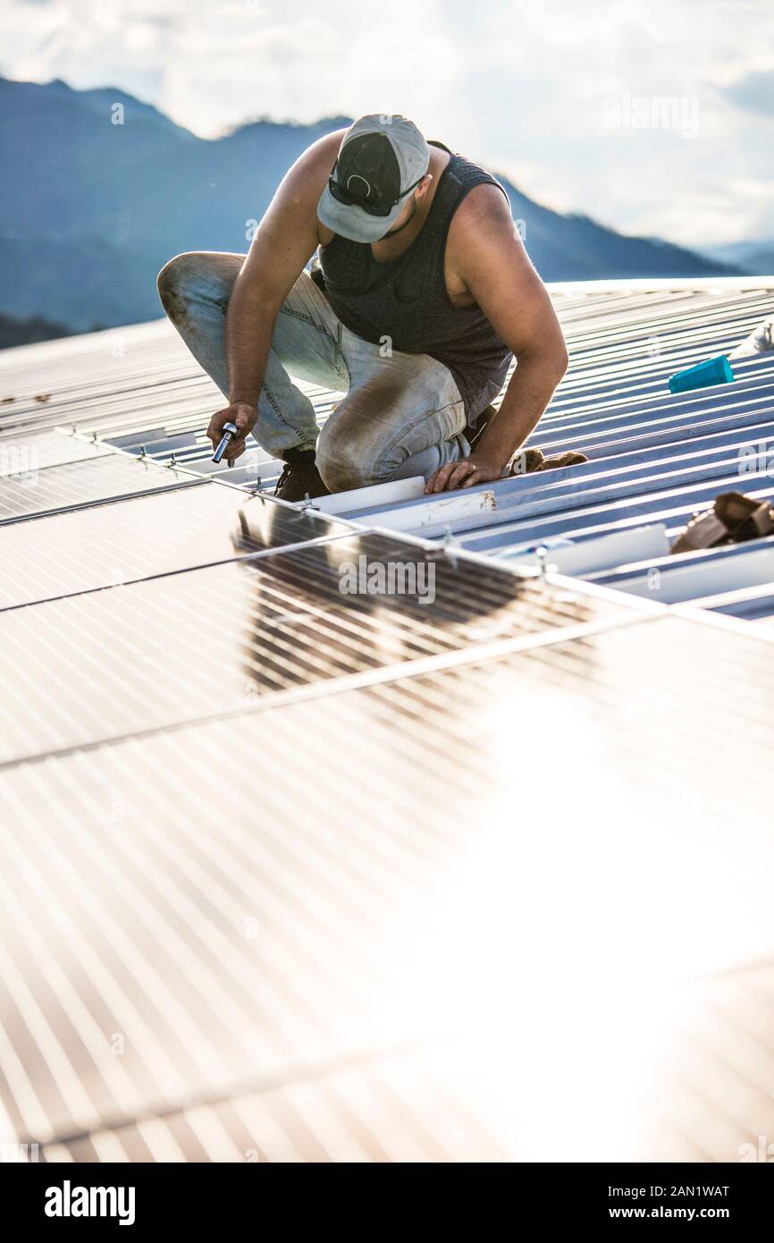 Il lavoratore utilizza l'attrezzo manuale per fissare i pannelli solari sul tetto dell'edificio. Foto Stock