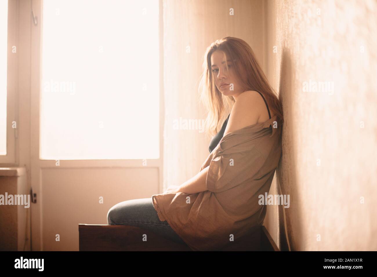 Ritratto di giovane donna seduta sulla testata del letto dalla finestra a casa Foto Stock