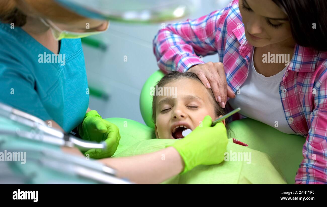 Spaventata bambina in visita dal dentista, mom calming lei, denti regolari checkup Foto Stock