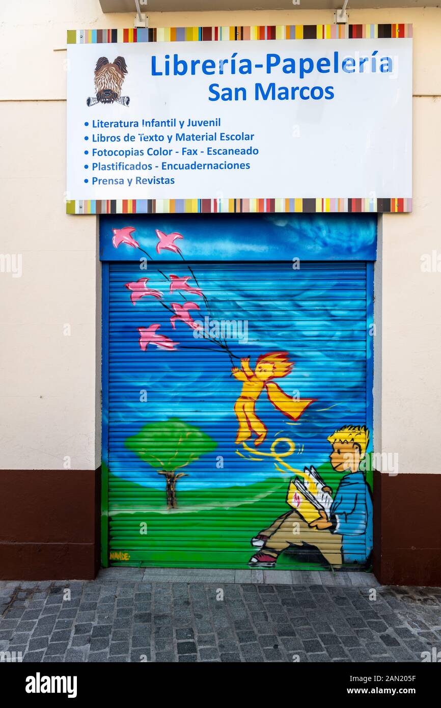 Un murale colorato di un bambino che legge un libro dipinto sulle persiane di una libreria / cancellatori in Plaza de San Marco. Siviglia Foto Stock