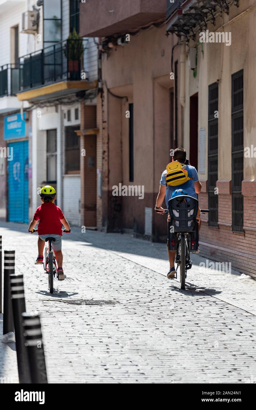 Gita in bicicletta con la famiglia. Un padre prende il figlio e la figlia per un giro in bicicletta intorno alle strette strade della vecchia Siviglia. Foto Stock