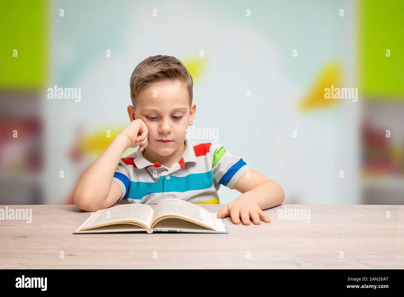Ragazzo legge un libro con il suo braccio poggiando sulla sua guancia. concetto di apprendimento pesante, e all'inizio del carico di lavoro per i bambini. Vista frontale, spazio di copia Foto Stock