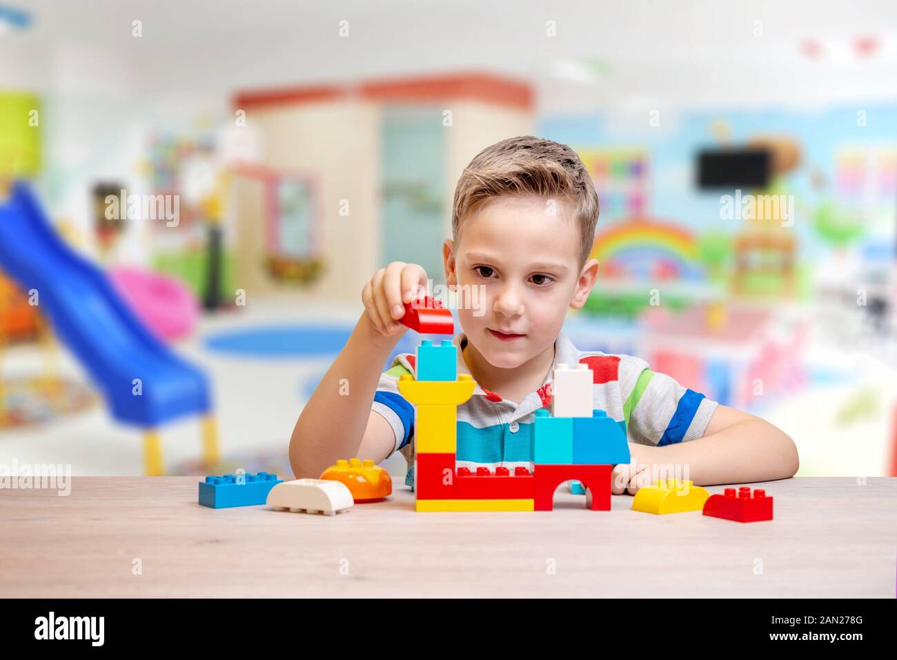 Ragazzo gioca con mattoni. Concetto di bambini per lo sviluppo delle capacità motorie e immaginazione. Sala giochi per bambini in background Foto Stock