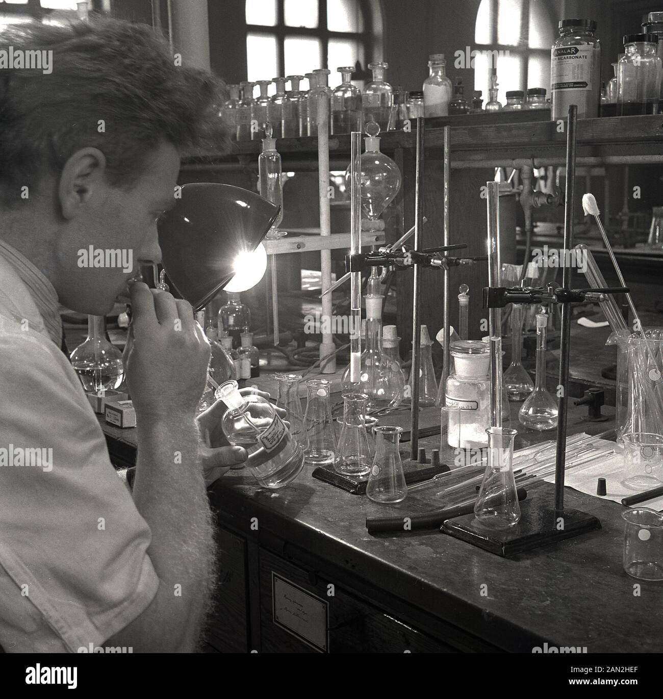 Degli anni Cinquanta, storico, maschio scienziato di ricerca in un laboratorio presso Università di Leeds a un banco da lavoro servendosi di contenitori in vetro per mescolare i prodotti chimici. Foto Stock