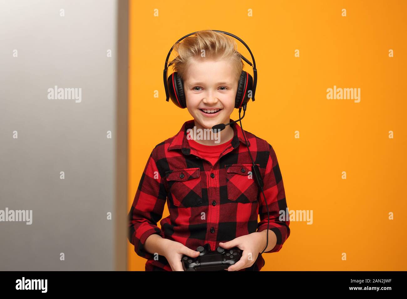 Bambino ragazzo gioca video giochi in cuffie. Giovane bel ragazzo caucasico sorridente nella camicia rossa sullo sfondo giallo. Orizzontale, dritto. Foto Stock