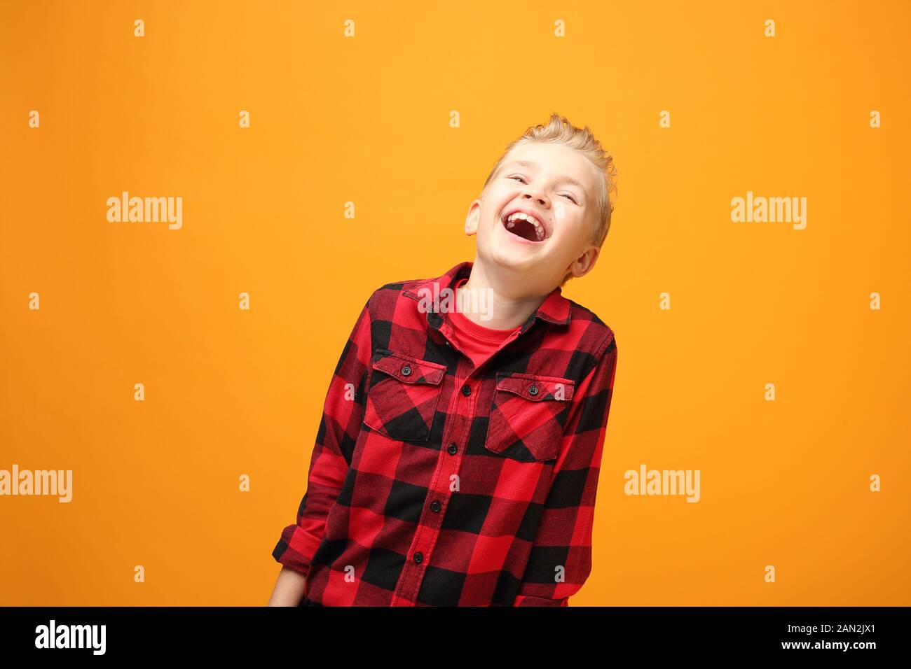 Felicità e gioia, emozioni di un bambino. Giovane bel ragazzo caucasico sorridente nella camicia rossa sullo sfondo giallo. Orizzontale, dritto. Foto Stock
