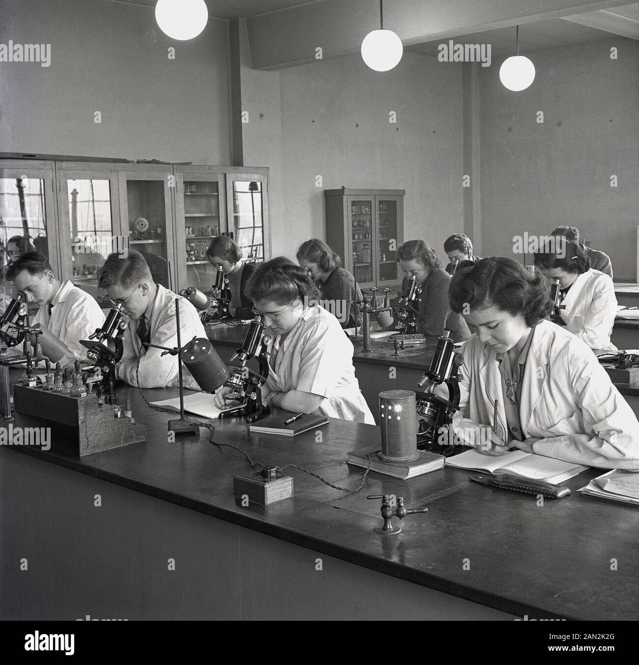 1948, storico, bianco-rivestita la scienza gli studenti in aula, seduti a banchi di lavoro con microscopi e prendendo appunti, Università di Leeds, Inghilterra. Foto Stock