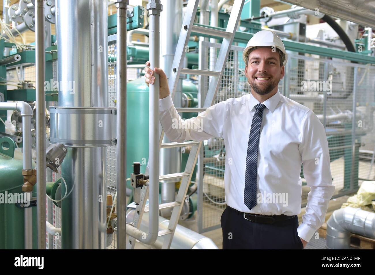Ritratto di un successo imprenditore sorridente/ tecnico sul sito in uno stabilimento industriale con casco Foto Stock