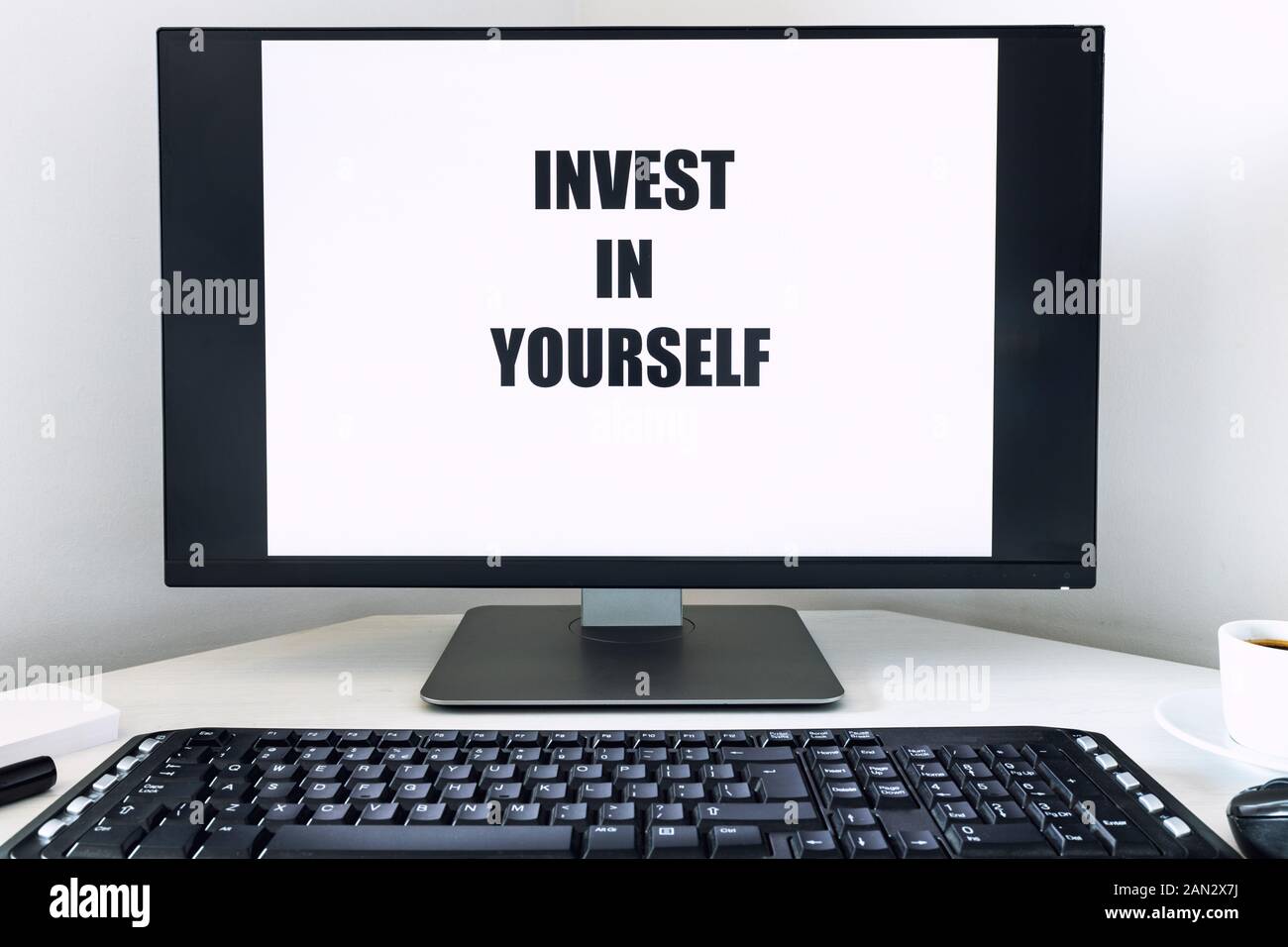 Testo visualizzato sul monitor, Invest in Te Stesso. Una scrivania con tastiera, accessori per ufficio e una tazza di caffè. Il concetto di personale e di professata Foto Stock